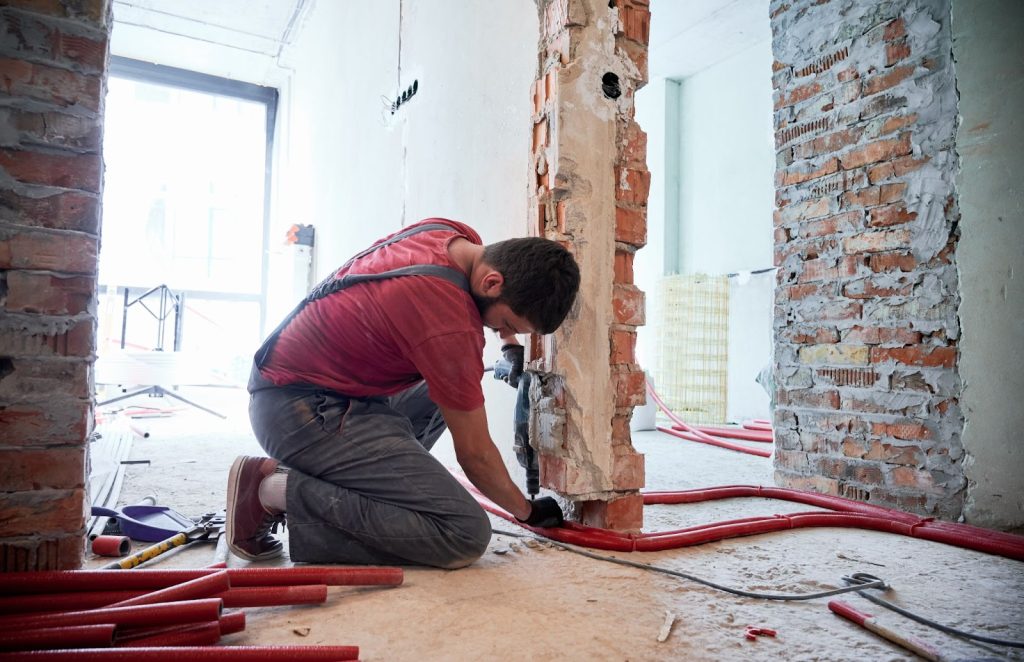 A man repairing a wall in an unfinished room, focusing on water mitigation and restoration