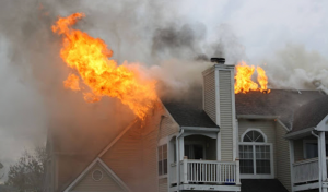 A house with flames shooting out of the roof, showing fire damage.
