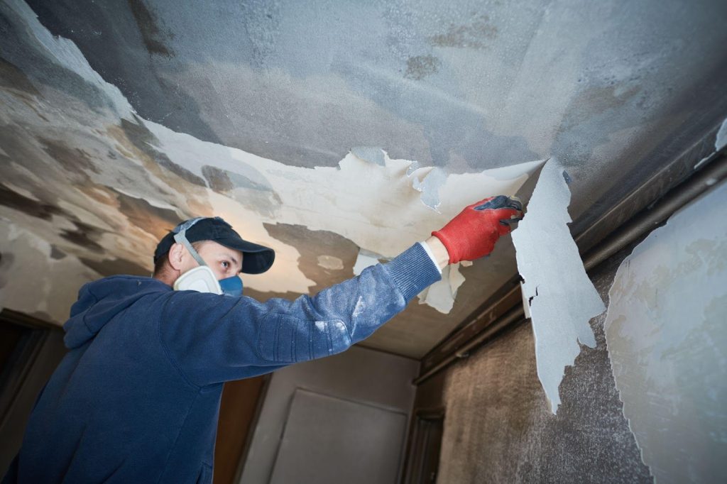 A man in a blue shirt and red hat painting the ceiling with a brush