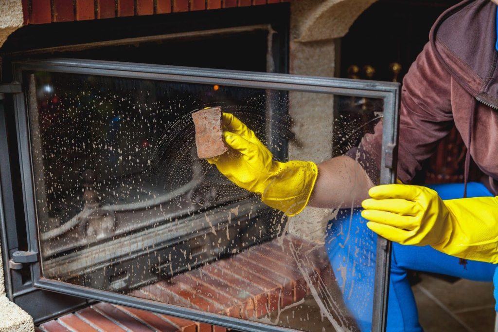A person in gloves cleaning a fireplace, removing ashes and scrubbing carefully