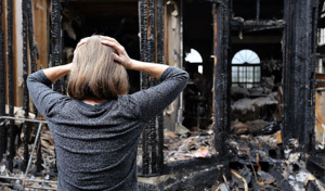 A woman standing in front of a burned house, surveying the damage and contemplating the aftermath.