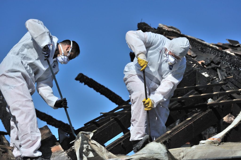 Two men in protective clothing conducting fire damage cleanup and restoration on a building.