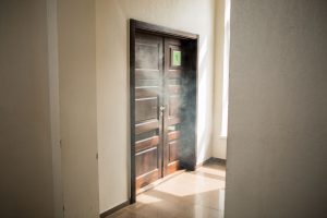 A door emitting smoke, indicating potential smoke damage and soot residue surrounding the area.