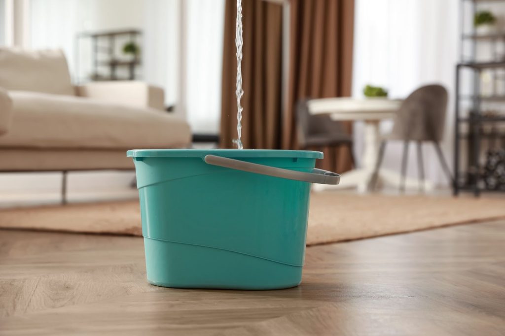 A bucket with a handle on the floor next to a couch.