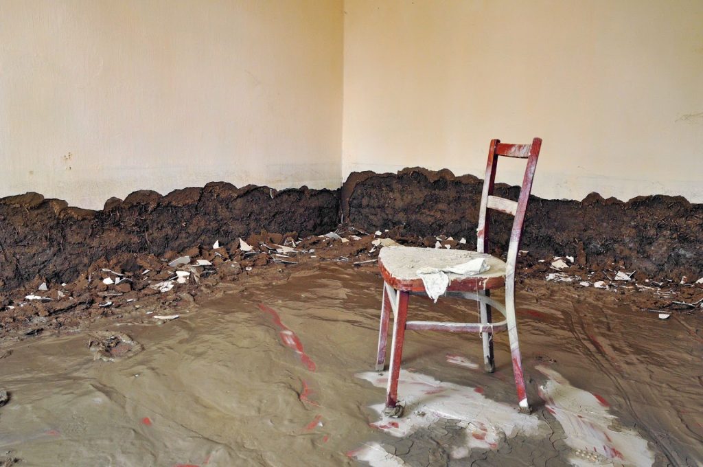 A chair surrounded by mud and dirt in a room, illustrating the aftermath of flooding in Utah.